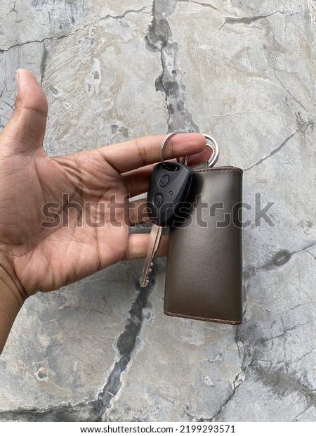 human hand holding car keys and leather hanger\
against gray wall\
background
