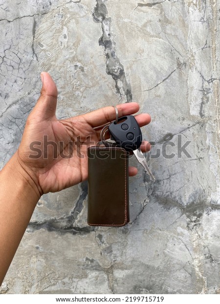 human hand holding car keys and leather hanger\
on gray wall background