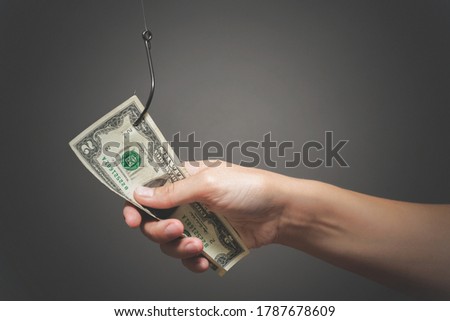 Human hand is holding a dollar on the fishing hook close up on gray background.