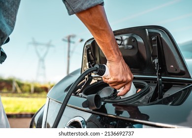 Human hand is holding electric car charging connect to electric car.