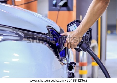 Human hand is holding Electric car, Plug the charger access to vehicle electrification
