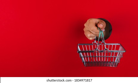 Human Hand Holding Empty Shopping Cart On Red Background. Christmas Holiday. Shopping Sales Banner. Paper Cut Circle. Text Space