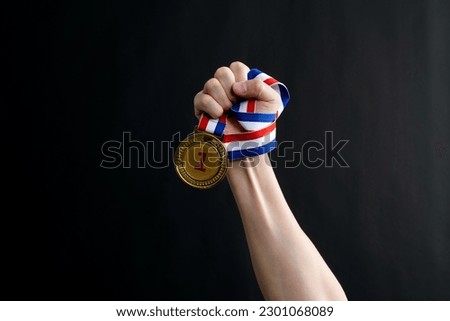 Human hand holding gold medal on black background.