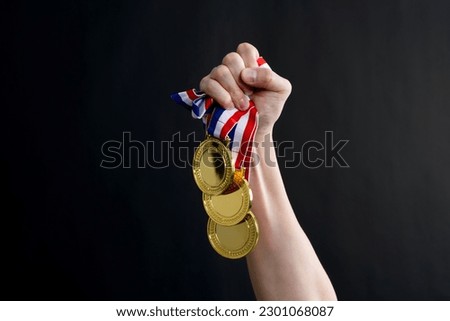 Human hand holding gold medals on black background.