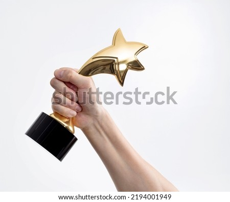 Human hand holding golden star trophy.