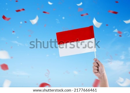 Human hand holding an Indonesian flag with a blue sky background. Indonesian independence day