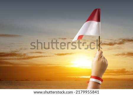 Human hand holding an Indonesian flag with a sunset sky background. Indonesian independence day
