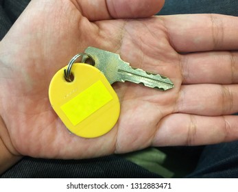 Human Hand Holding A Key With Empty Yellow Tag Sign Space.