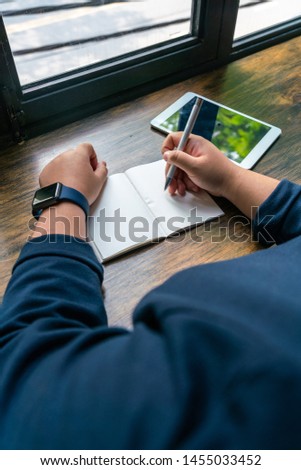 Human hand holding pen and writing next to tablet