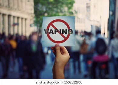 Human hand holding a protest banner stop vaping message over a crowded street background. Banning flavored vaping products to discourage people from smoking electronic cigarettes. Health risk concept.