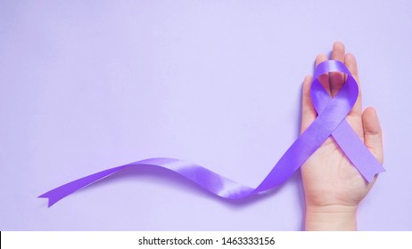 Human hand holding purple ribbon awareness on purple background. Symbol is used to raise awareness for Alzheimer's disease, Epilepsy, Pancreatic cancer, Thyroid cancer and Lupus. Copy space.