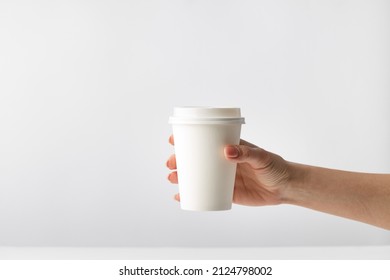 Human hand holding a white mockup closed paper coffee cup on a solid white background, morning in the coffeeshop, fast delivery 