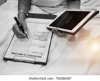 The human hand with IV solution is writing on the  Insurance Claim Form with pen and holding Ipad in hand ,in black and with tone ,blurry light around