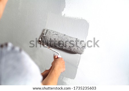 Human hand with large roller of paint begins to paint a white wall handicraft master painter training contrast color sample color test tool renovation gray silver craftsman
