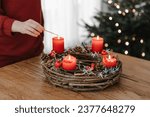 Human hand lighting all four candles on rustic advent wreath on Christmas Eve. Celebrating cozy winter time at home.