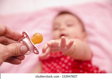 Human hand offering pacifier to out of focus blurred baby.