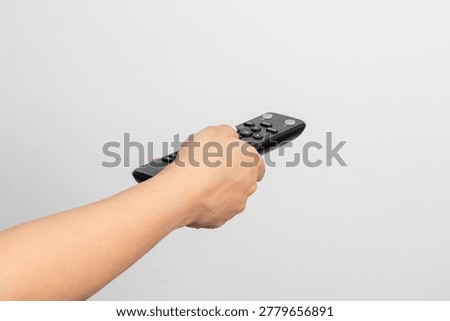 Human hand operating a black universal remote control against a white background