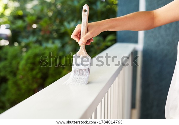 Human hand painting a house deck\
handrail, doing home improvement by refreshing the paint of the\
wooden structure at the house entry. Fresh wet white\
paint.
