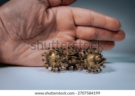 A human hand is placed behind three bronze-colored virus figurines with animated facial features suggesting defense or confrontation.
