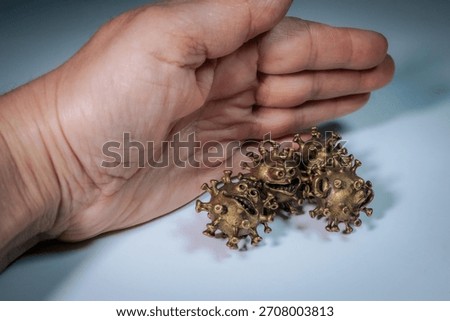 A human hand is placed behind three bronze-colored virus figurines with animated facial features suggesting defense or confrontation.