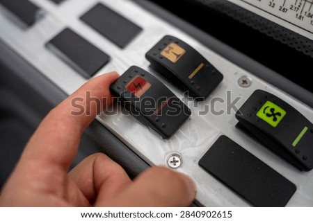 Human hand pressing toggle switch with electronic lightning icon on vehicle dashboard panel inside machinery cabin.