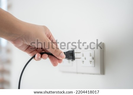 Human hand put in or out electric plug in the socket to connect the devices. Household technology in use of human hand. Using of electric plug concept of safety, or environmental conservation.