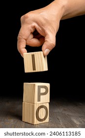 A human hand put a stack of wooden cubes with IPO letters on a wooden table. Stock investment concept