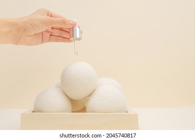 Human Hand Putting Aroma Oil On Wool Dryer Balls On Wooden Podium On Beige Background. Eco Friendly Laundry Supplies. Alternative Drying Of Linen. Still Life. Text Space. 