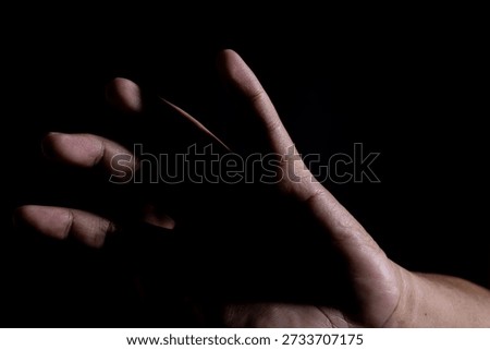 Human hand reaching forward in dramatic low light on black background, symbolizing desire, opportunity, uncertainty, and emotional connection concept.