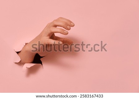 Human hand reaching through a torn hole in pink paper. Creative studio shot with copy space for design and print.