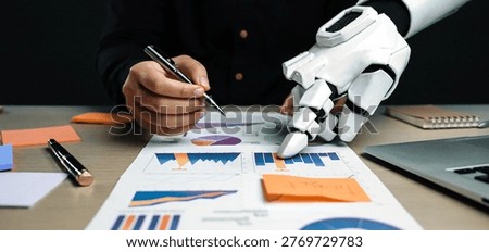 A human hand and a robotic hand work together on data analysis, showcasing the synergy between technology and human intellect in a modern workspace.Noogenesis