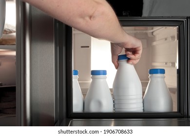 Main humaine prenant une bouteille de lait d'un réfrigérateur passant par la petite porte