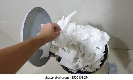 Human Hand Throwing The Used White Tissue Paper In To A Foot Pedal Toilet Bin.Toilet Bin Overflowing With Used And Dirty Tissue Paper. 