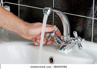 Human Hand Turn On Faucet At Bathroom. Stream Of Pure Water From Tap