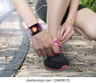 human hand tying shoelaces wearing bright pink watchband touchscreen smartwatch with red health icon on forest trail background