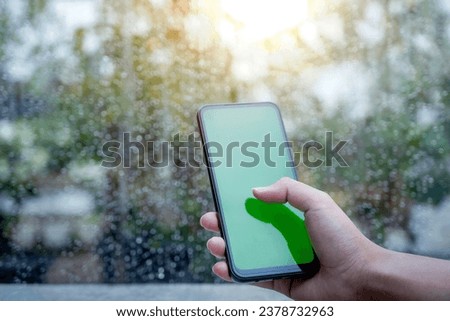 Human hand using a mobile phone with a blank screen with a clear window and raindrop background. Blank screen for copy space