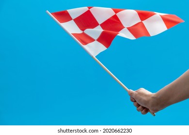 Human Hand Waving Checkered Flag On Blue Background.