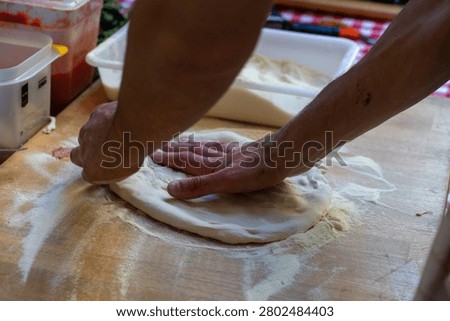 Human hands actively shaping pizza dough during the preparation of a fresh homemade pizza. Captured in a food service setting, the image showcases the essential steps of traditional pizza production, including dough handling, ingredient placement, and artisan cooking methods. The photograph represents culinary expertise, restaurant food preparation, and authentic pizza-making traditions.