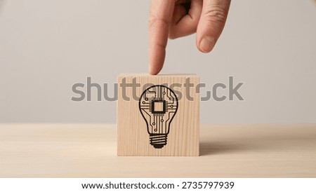 A human hand's finger points down onto a wooden block featuring a light bulb with an integrated circuit design, symbolizing innovation and technology and the spark of an idea.