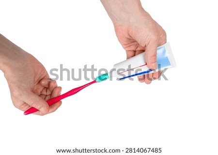 human hands gently squeeze mint green toothpaste from a plastic white tube onto the bristles of a red plastic toothbrush on a white isolated background
