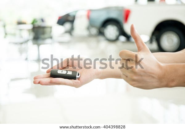 Human hands giving thumbs up with car key in\
car shoowroom