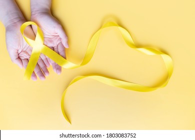Human Hands Giving Yellow Gold Ribbon Awareness Symbol For Support Suicide Prevention, Endometriosis, Sarcoma Bone Cancer, Bladder Cancer, Liver Cancer And Childhood Cancer Concept.