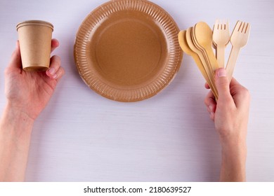 Human Hands Hold Coffee Cup And Wooden Spoon, Fork Near Brown Empty Paper Plate