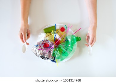 Human Hands Hold A Fork And Spoon Over A Plate Of Plastic Trash. The Concept Of Environmental Pollution With Plastic Waste And The Danger Of Microplastics For Human Health, Microplastic In Food.