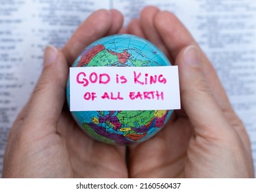 Human hands hold handwritten verse quote, God is King of all earth upon world globe and open Holy Bible Book. A close-up. Christian biblical concept of praise, worship, glory to the LORD. Top view.