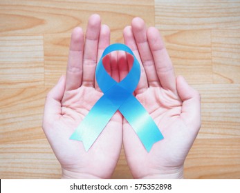 Human hands holding light blue ribbon awareness on wooden background. Men's health campaign concept. Symbol is used to raise awareness for Prostate cancer, Achalasia and Adrenocortical carcinoma.