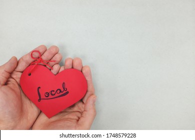 Human hands holding a red heart tag with handwritten word local. Support, promote, buy, shop and love local business concept. Gray background, top view.
