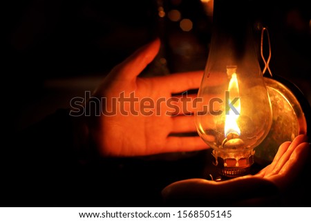 Human hands next to litted oil lamp in a gloom dark night