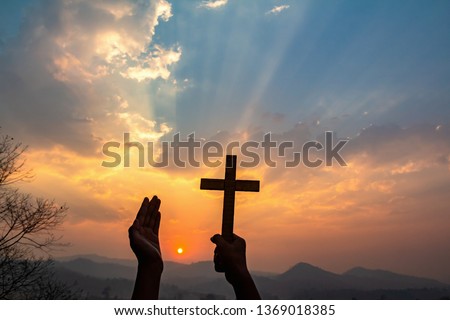 human hands praying to the GOD while holding a crucifix symbol with bright sunbeam on the sky