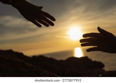 Human hands reaching out for help, support, and connection, silhouetted against a golden ocean sunset, embodying concepts of hope, teamwork, and assistance in a challenging environment